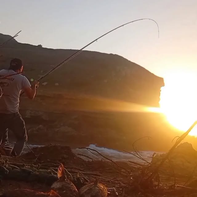 Di Sargos com a cana na mão, a peixe ao lado, ao pôr do sol na Ericeira